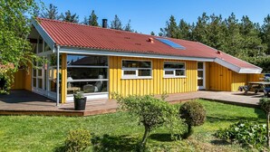 Keltainen talo, jossa on punainen katto, suuret ikkunat ja katettu kuisti.