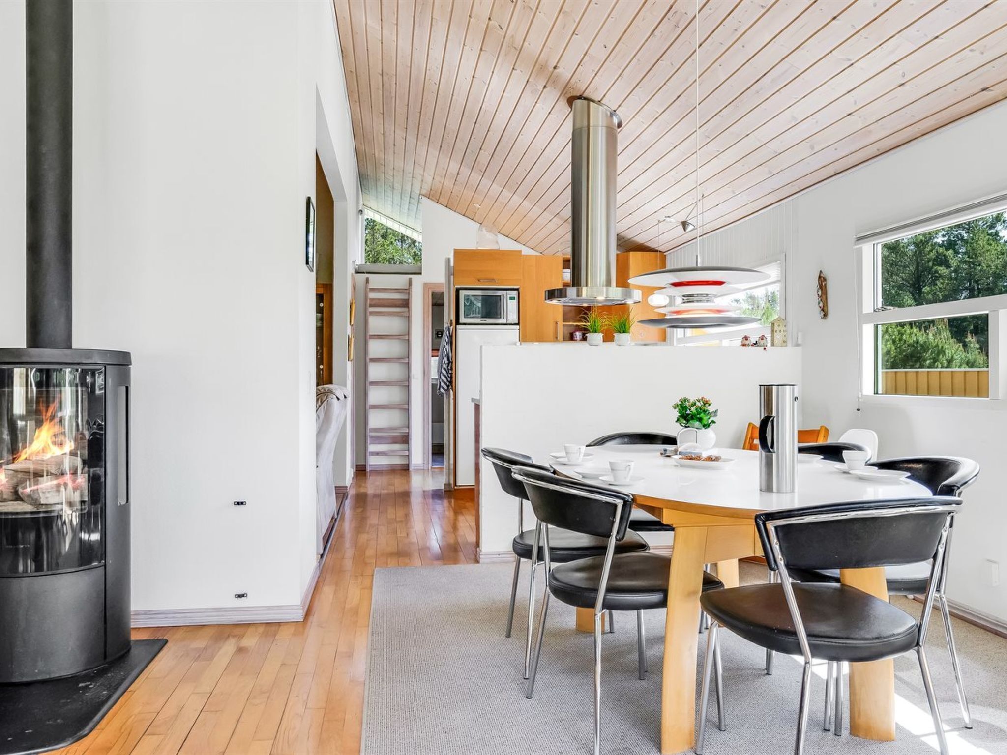 A modern kitchen with a central island, a dining area with a table and chairs, and a wood-burning stove.