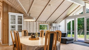 A dining area with a wooden table and chairs, a sofa, and a large window with a view of greenery. - "Gottfrede" - 600m from the sea by Interhome (Løkken)
