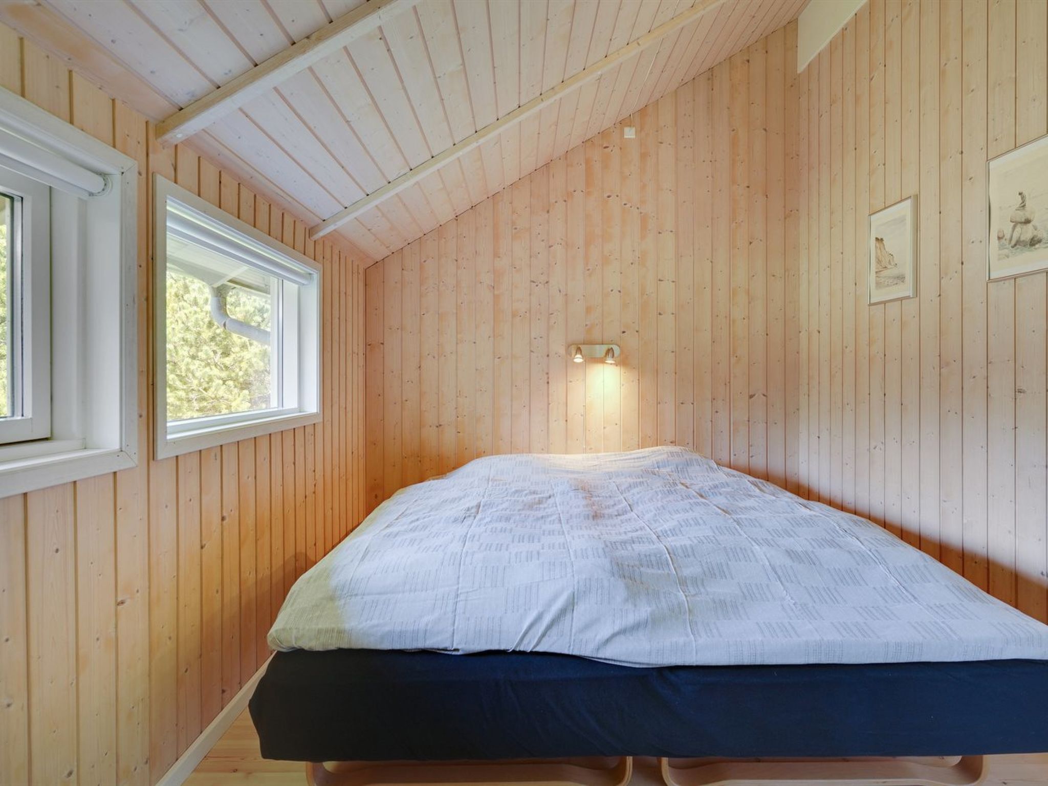 Una stanza con rivestimento in legno, un letto, due finestre e illuminazione a parete.