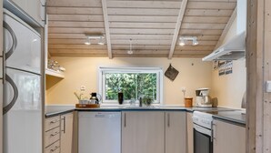 A modern kitchen with wooden cabinets, a built-in dishwasher, a stove, and a window overlooking greenery. - "Gottfrede" - 600m from the sea by Interhome (Løkken)