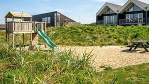 Une propriété située en bord de mer, dotée d’une structure de jeux en bois, d’un toboggan vert et d’une table de pique-nique.
