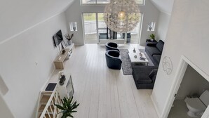 Un loft moderne avec de hauts plafonds, de grandes fenêtres, un lustre central et un coin salon confortable.
