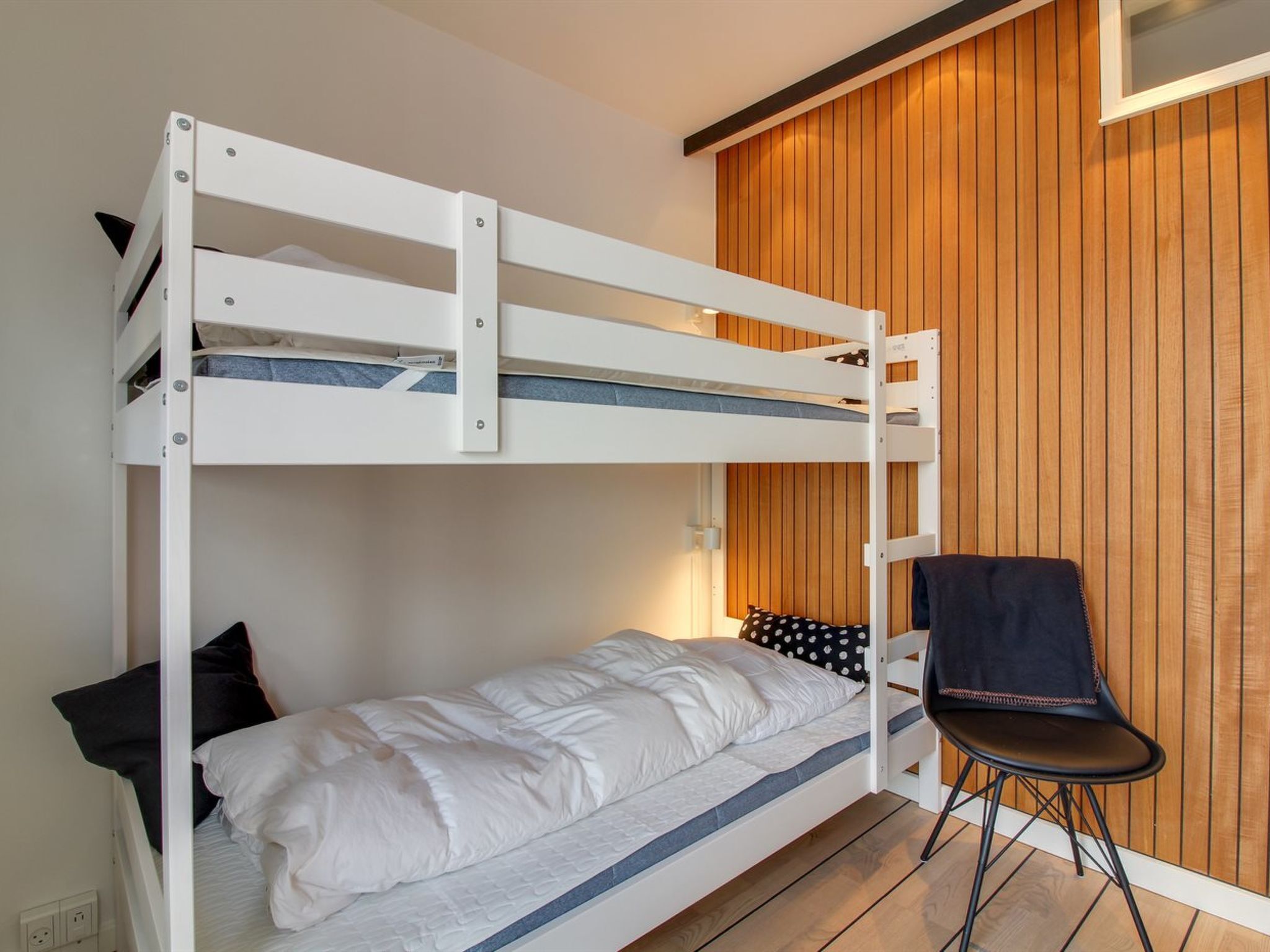 A bunk bed with a single bed below, a chair, and a wooden panel wall.