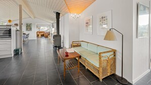 Uma cozinha espaçosa com um fogão grande, uma área de refeições com mesa e cadeiras de madeira, e um espaço de estar acolhedor com sofá e abajur.