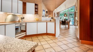 A modern kitchen with wooden cabinets, a granite countertop, and a dining area with a view of greenery. - "Tule" - 1.2km from the sea by Interhome (Blåvand)