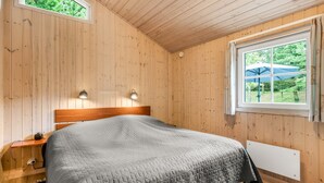A bedroom with a wooden ceiling, a bed with a quilted blanket, bedside lamps, a window with an umbrella, and a view of greenery outside. - "Tule" - 1.2km from the sea by Interhome (Blåvand)