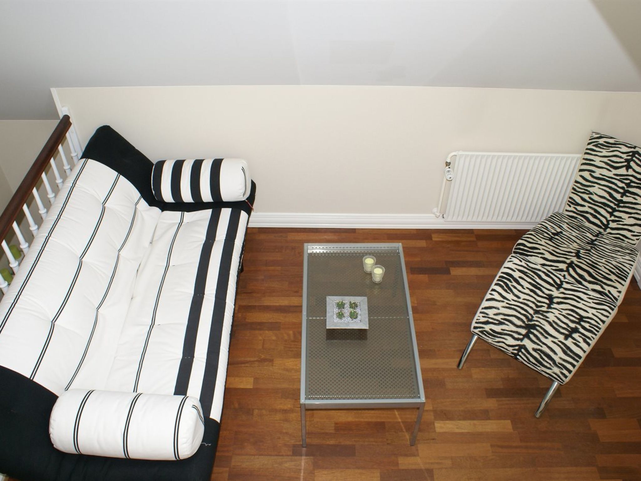 A living room with a striped sofa, a zebra-patterned chair, and a glass coffee table with a small plant.