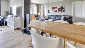 Ein modernes Wohnzimmer mit einem Holzesstisch, weißen Stühlen, einem grauen Sofa und einem schwarzen Kamin.