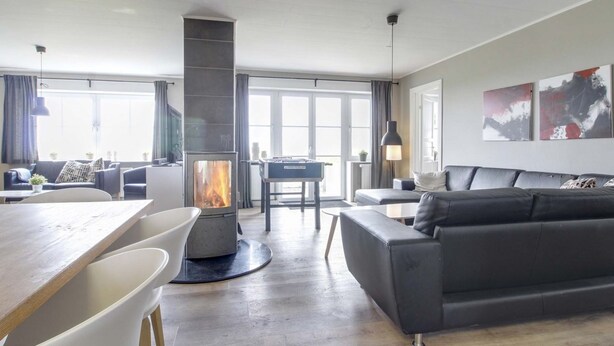 Ein modernes Wohnzimmer mit Kamin, Sofa, Esstisch und Blick ins Freie.