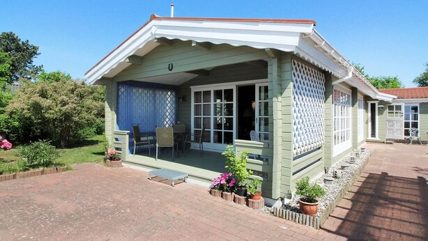 Einbungalow mit Veranda, überdachter Terrasse und kleinem Garten mit Kübelpflanzen.