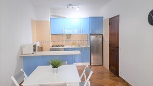 Uma cozinha compacta com armários azuis, bancada branca, micro-ondas, fogão e geladeira.