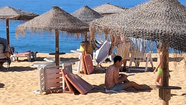 Uma praia com guarda-sóis de palha, espreguiçadeiras e um calçadão de madeira.