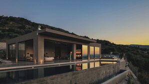 Ein modernes Haus mit großer Glasfassade, einem Swimmingpool und Blick auf die umliegenden Hügel.