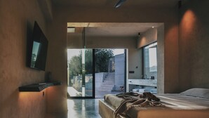 Ein modernes Schlafzimmer mit einem großen Bett, einem flachbildfernseher an der Wand und einer Glastür zum Außenbereich.
