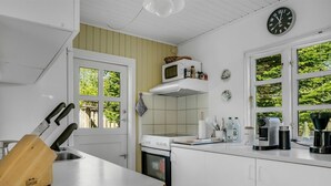 A modern kitchen with white cabinets, a microwave, a stove, and a coffee maker. There are windows with a view of greenery outside. - "Ingobert" - 50m from the sea by Interhome (Hals)