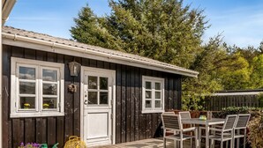 A wooden deck with a table and chairs, a white door, and a window with a wreath. - "Ingobert" - 50m from the sea by Interhome (Hals)