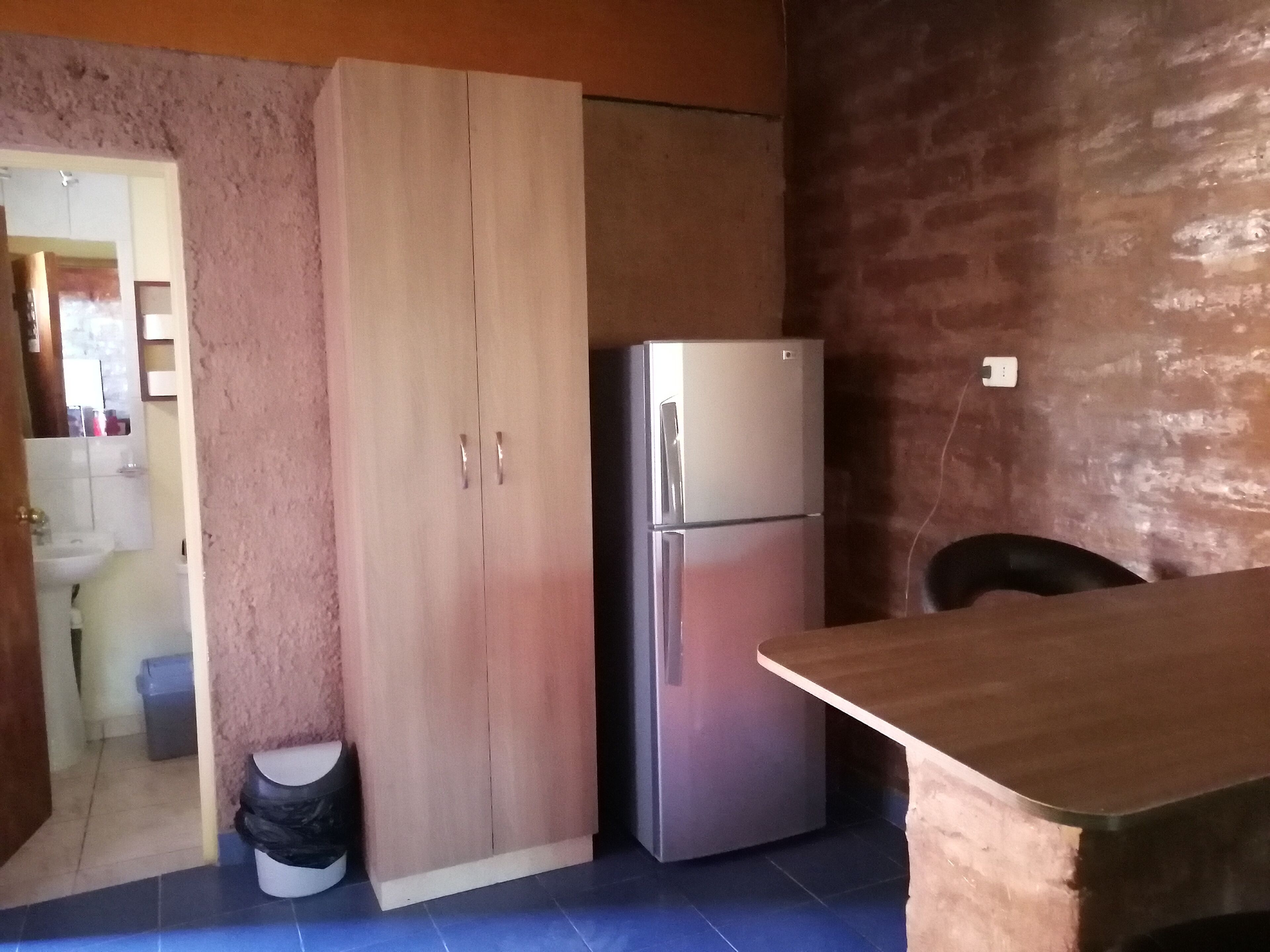A kitchen with a wooden cabinet, a stainless steel refrigerator, and a tiled floor.