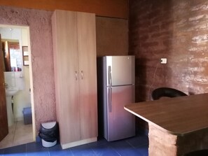 A kitchen with a wooden cabinet, a stainless steel refrigerator, and a tiled floor. - HOSTAL SOLOR (San Pedro de Atacama)