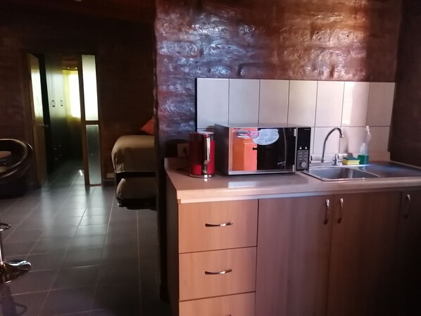 A modern kitchen with a built-in microwave, a sink, and wooden cabinets. - HOSTAL SOLOR (San Pedro de Atacama)