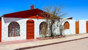 Un edificio con tejado rojo, paredes blancas con diseño de piedra y tres ventanas arqueadas con puertas de madera.