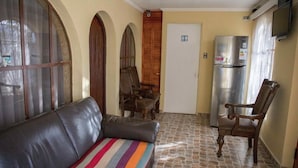 Una habitación con sofá de cuero, sillas de madera, un refrigerador y una puerta con un letrero.