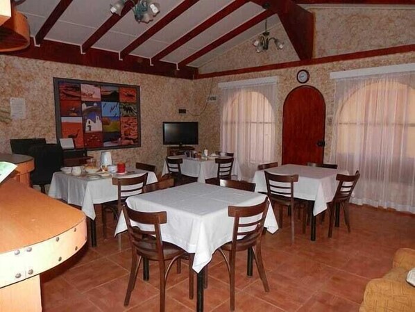 Un comedor con varias mesas y sillas, un televisor y un reloj en la pared.