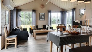 Une pièce chaleureuse et bien éclairée, avec un plafond haut, des poutres apparentes, un coin repas avec une table et des chaises, un canapé et un téléviseur.