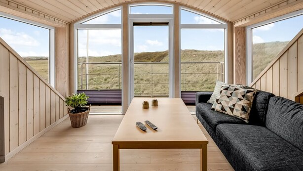 Een kamer met een houten plafond, grote ramen, een bank, een tafel en een plant.