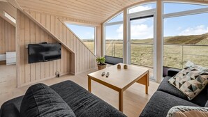 Een knus ingerichte kamer met een houten plafond, een flatscreen televisie aan de muur, een houten tafeltje en een bank met kussens.