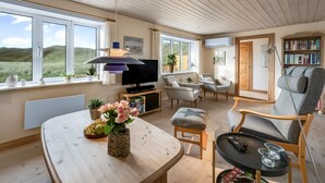 Een ruime woonkamer met een groot raam, een televisie, een boekenkast en een gezellige zithoek.