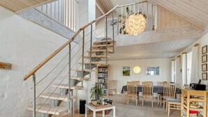 Een ruime woonkamer met een houten trap, een eettafel en een boekenkast.