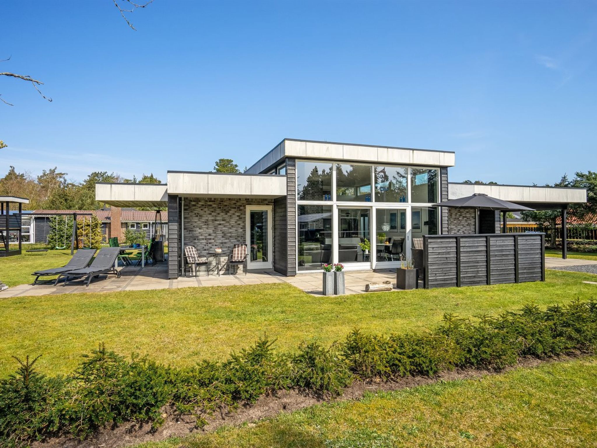 Ein modernes Haus mit einer Terrassenfläche, einer überdachten Sitzgelegenheit und einem umzäunten Garten.