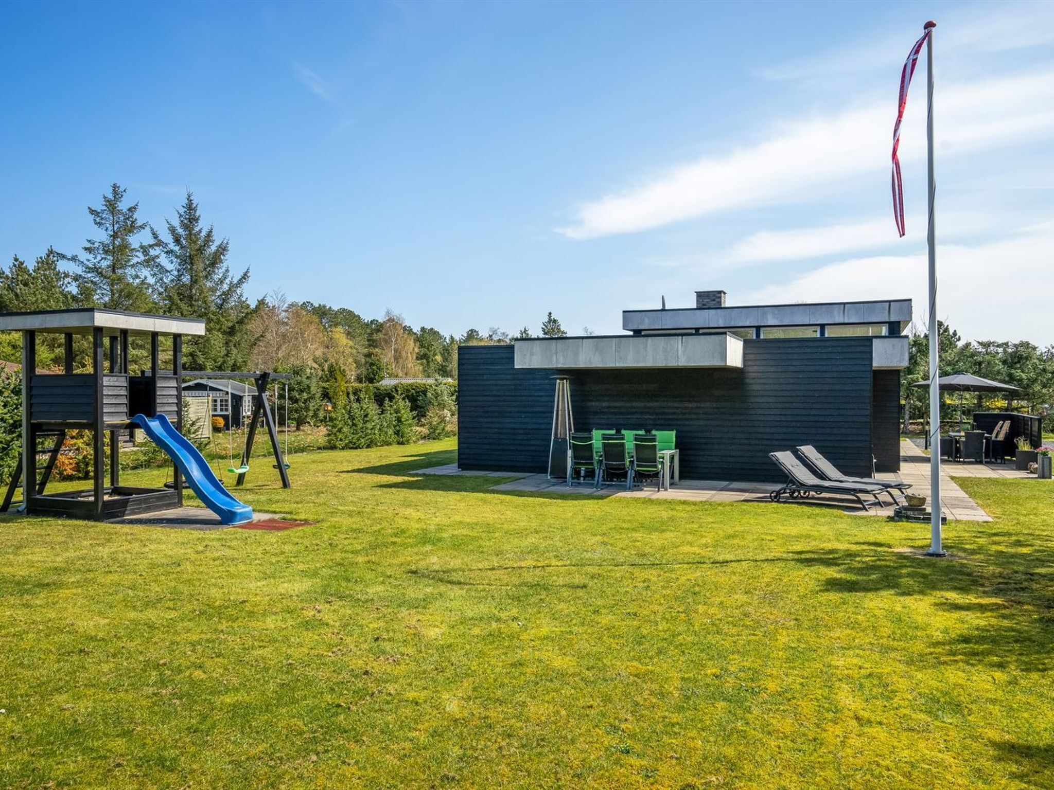 Ein moderner Außenbereich mit Spielplatz, überdachtem Sitzbereich und einer Fahnenstange.