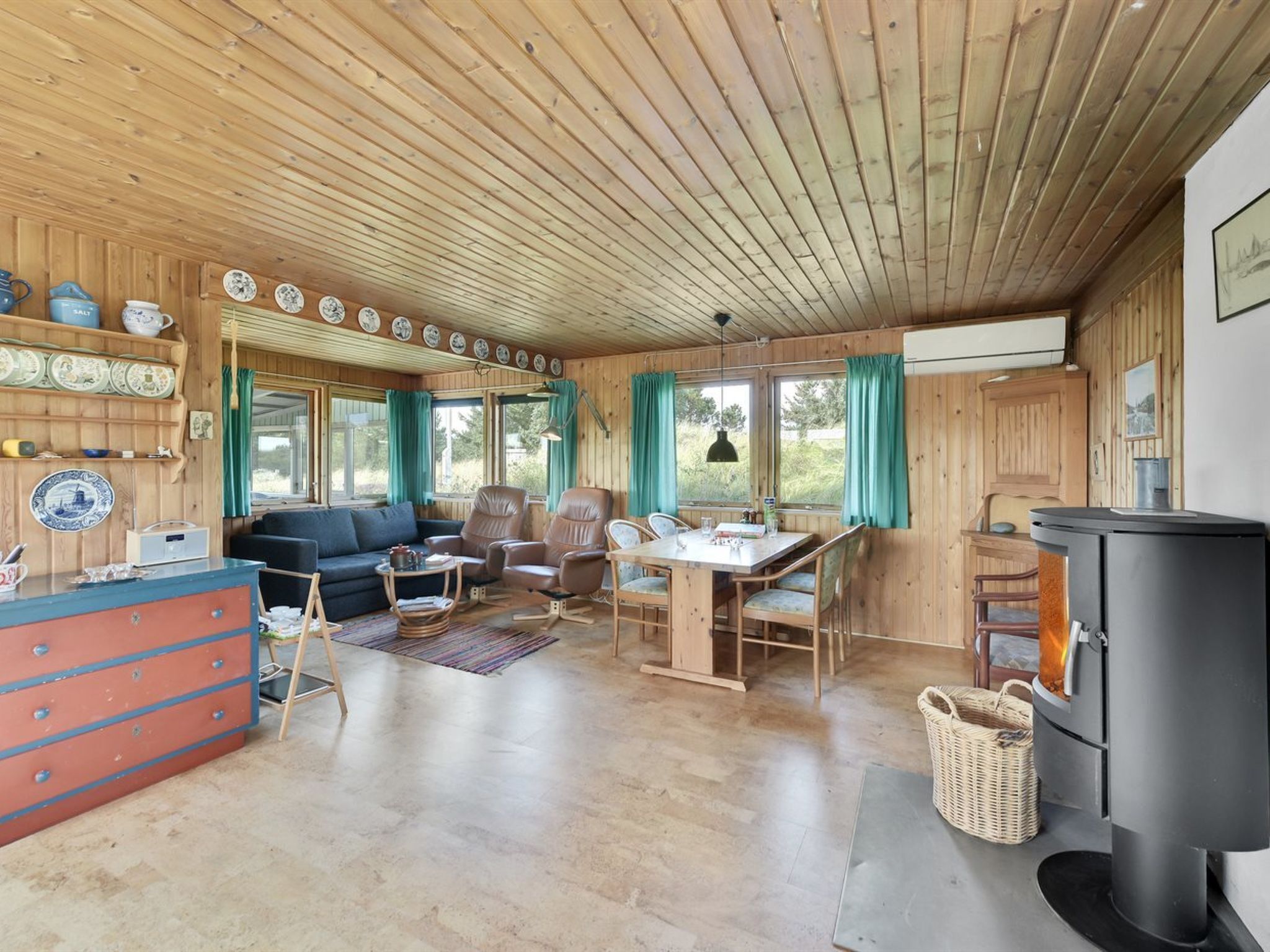 A cozy cabin interior with a wooden ceiling, a dining area, a sofa, and a fireplace.