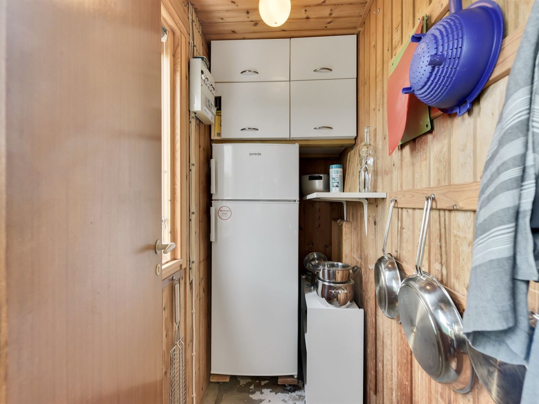 A compact kitchen with a white refrigerator, wooden cabinets, and a hanging pot rack.