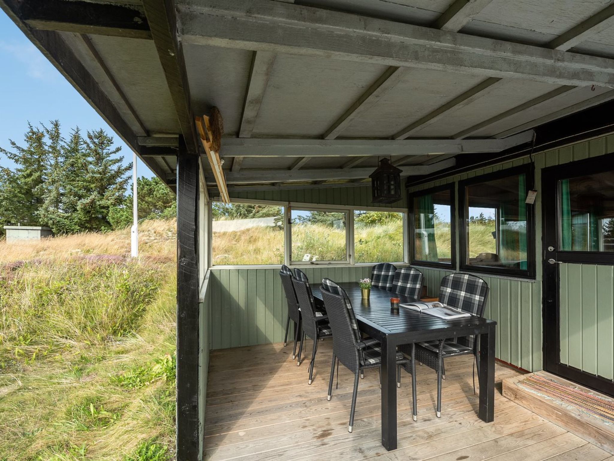 Een overdekt terras met tafel en stoelen, met uitzicht op een grasveld.