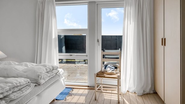 Ein Schlafzimmer mit Bett, einem Sessel und Blick durch eine Schiebetür auf einen Außenbereich.
