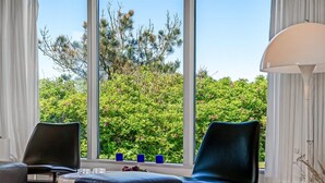 Ein modernes Zimmer mit zwei schwarzen Stühlen, einem weißen Tisch und einem großen Fenster mit Blick auf üppiges Grün und Bäume.