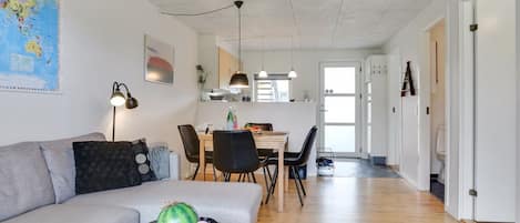 A modern living room with a grey sofa, a dining table with chairs, and a kitchen area in the background.
