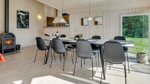 Een moderne eethoek met een houten plafond, een inbouwhoutkachel en een groot raam met uitzicht op een tuin.