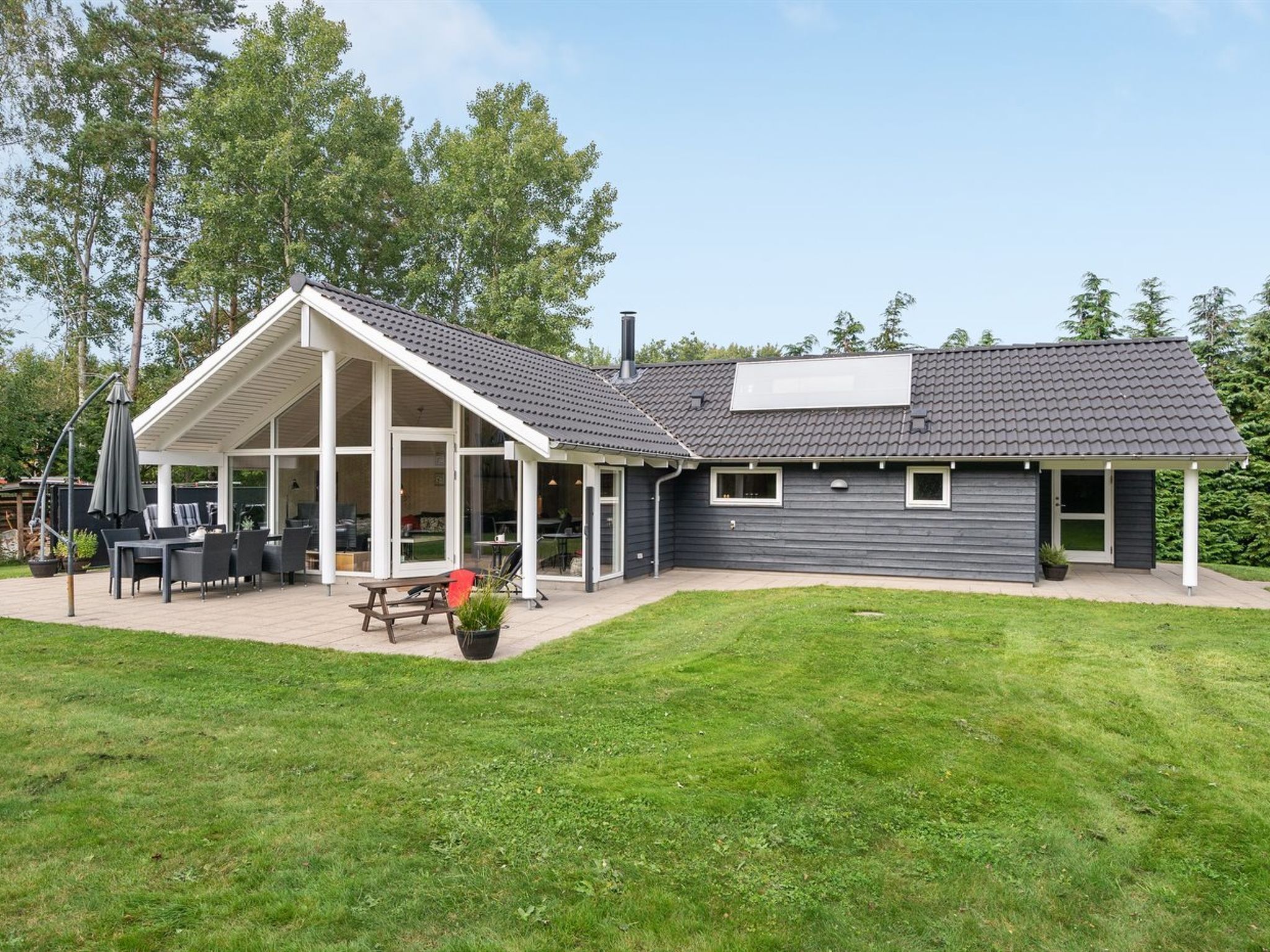 Une maison moderne dotée d’un patio couvert, d’un coin repas et d’une grande pelouse.