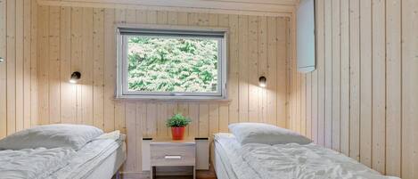 A room with two single beds, a small bedside table with a plant, and a window with a view of greenery.