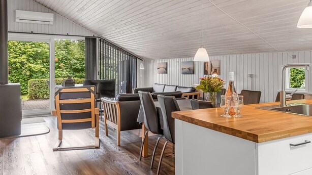 A modern kitchen with a wooden island, a dining area with a sofa and chairs, and a view of greenery outside. - "Corinna" - 28km from the sea by Interhome (Toftlund)