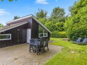 Een modern huis met een patio, compleet met een tafel en stoelen, omgeven door weelderige begroeiing.