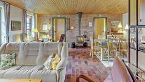 Een gezellige woonkamer met een metselstenen open haard, houten plafond en een eethoek met houten meubels.