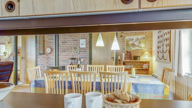 Een gezellig eetgedeelte met houten stoelen en een tafel, een bakstenen muur met kunstwerken, en een houten kast boven de tafel.