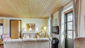 Een gezellige kamer met een bank, een televisie en een houten plafond.