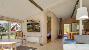 A cozy living room with a sofa, a table, and a TV mounted on the wall. There's a wooden door leading to another room, and a window providing natural light. - "Alisia" - 400m from the sea by Interhome (Hals)
