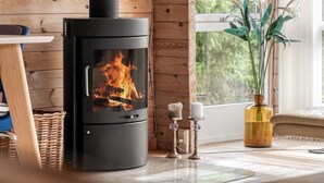 A wood-burning stove with a glass door, a wicker basket, a vase with flowers, and a window with a view of greenery. - "Jannus" - 550m from the sea by Interhome (Hals)